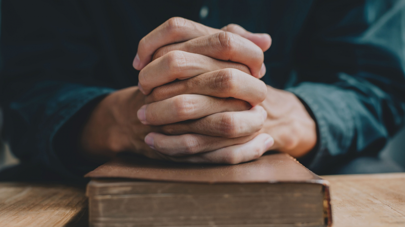 Hands of a man praying over a Bible represents faith and spirituality in everyday life. close up.